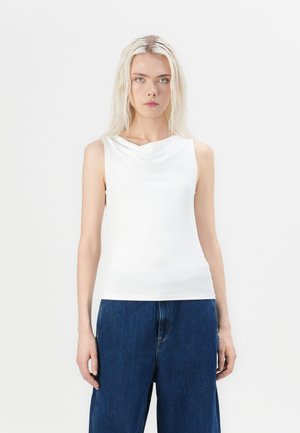 Haut sans manches blanc avec un col drapé et une texture lisse et extensible, associé à un jean bleu foncé ample.