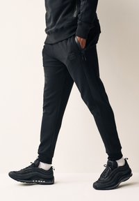 Sorte sweats med en tætsiddende design og elastiske manchetter, med lynlåslommer og diskret logo detalje. Båret sammen med sorte sneakers.