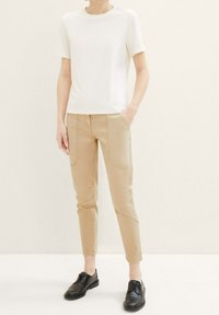 White short-sleeve t-shirt paired with beige tapered pants featuring contrast stitching, alongside black lace-up shoes on a light background.