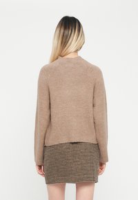 Brauner Strickpullover mit hohem Kragen, geripptem Saum und langen Ärmeln, kombiniert mit einem karierten braunen Rock. Weiche Textur, minimalistisches Design.