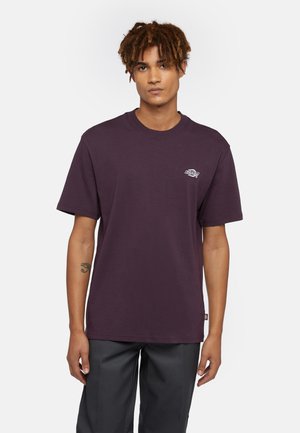 Camiseta de algodón color burdeos con escote redondo y mangas cortas, que presenta un pequeño detalle de logo en la parte superior izquierda del pecho.