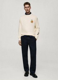 Felpa beige con logo hamburger di New York, abbinata a pantaloni blu navy e scarpe nere. Presenta collo rotondo e maniche lunghe.