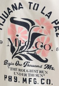 Cremefarbener Baumwollstoff mit schwarzen und pinkfarbenen Blumenmotiven. Der Text beinhaltet "TIJUANA TO LA PAZ", "MFG. CO." und "THE ROUGHEST RUN UNDER THE SUN."