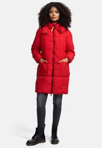 Red puffer coat with a high collar, zippered front, and elastic cuffs. Features two front pockets and a quilted texture. Worn over dark jeans and black boots.