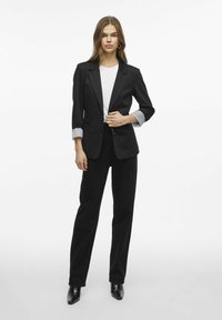 Černý blazer s jasně šedými pruhovanými manžetami, přizpůsobený střih, spárovaný s černými kalhotami a bílým tričkem; hladký materiál, bez viditelných vzorů.