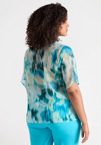 Blusa trasparente con maniche corte, caratterizzata da un motivo astratto blu e giallo; scollatura rotonda; tessuto leggero con una superficie liscia.