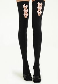 Bas résille noirs jusqu'à la cuisse avec six nœuds roses le long de chaque côté extérieur des jambes ; texture lisse et ajustement serré ; associés à des chaussures à talons hauts noires.