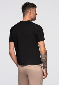 Sort kortærmet T-shirt med rund halsudskæring og raglan ærmer; har en glat tekstur og et diskret logo på kanten.