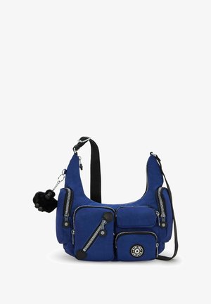 Blaues Schultertasche mit mehreren Reißverschlusstaschen, schwarzen Akzenten und einem pelzigen Anhänger. Hergestellt aus glattem Stoff mit kontrastierenden Nähten.