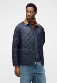 Ναυτικό μπουφάν με λουστρινένιο καφέ γιακά από κορντόρι, που διαθέτει μπροστινή τσέπη με κούμπωμα και φερμουάρ, σε συνδυασμό με ένα μεσαίο στρώμα με ζιβάγκο.