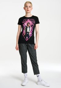 Black cotton T-shirt featuring a colorful 'Star Wars' graphic with a diamond pattern, paired with gray checkered pants and white sneakers.
