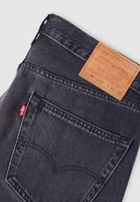 Jean Levi's lavage foncé plié pour montrer la poche arrière et le patch en cuir beige indiquant la taille 32 par 32 et le style 501 coupe ample.