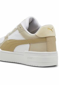 Fehér és bézs sneaker, bőrből és velúrból készült textúrákkal, lekerekített formával, párnázott szegéllyel és arany Puma logóval a hátsó részén.