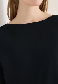 Nahaufnahme einer Person, die ein schwarzes Rundhals-T-Shirt trägt und einen Teil des Halses, der Schulter und hellbraunes Haar zeigt.