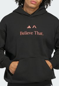 Felpa nera con cappuccio realizzata in tessuto morbido, con una grande scritta e logo rosa "Believe That." sulla parte anteriore. Include una tasca frontale.