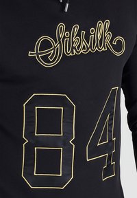 Felpa sportiva nera con cappuccio caratterizzata dal marchio "Siksilk" ricamato in oro e grandi numeri "84" in un design a contrasto. Tessuto testurizzato.