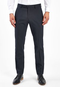 Pantalones de vestir navy de corte recto, fabricados en tejido suave con cierre de botón y bolsillos laterales, combinados con zapatos de cuero negros.