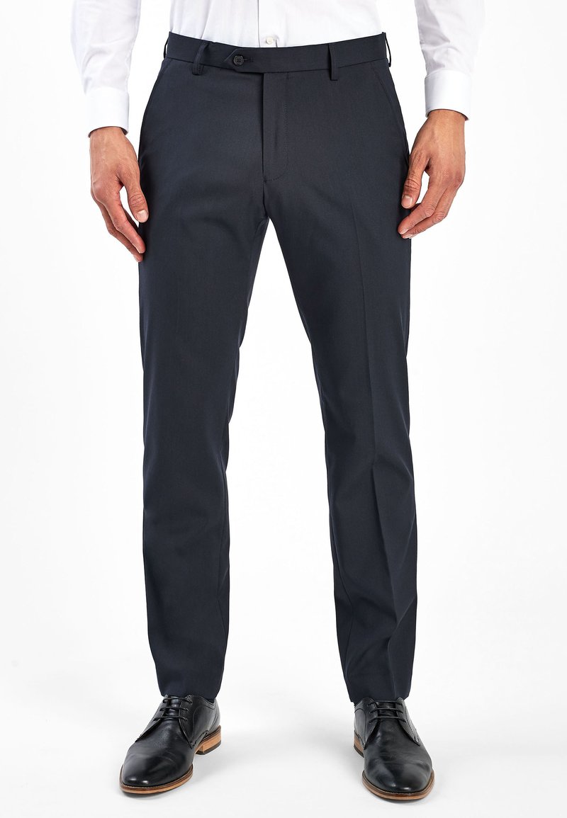 Pantalones de vestir navy de corte recto, fabricados en tejido suave con cierre de botón y bolsillos laterales, combinados con zapatos de cuero negros.
