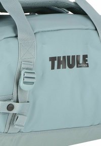Bolsa Thule azul claro con correas texturizadas, logotipo negro y hebilla ajustable. Material duradero con un acabado suave y costuras reforzadas.