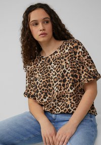 Leopardprint top met korte mouwen in bruin en zwart. Zachte stof met een relaxte pasvorm, ronde halslijn en opgerolde mouwen. Gekleed met lichtblauwe jeans.