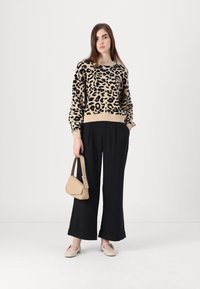 Bežani pulover s crnim leopard uzorkom, crne široke hlače, bež torba i svijetle cipele. Glatka tekstura, ležeran kroj i opušteni dizajn.