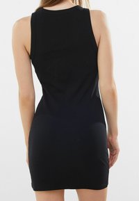 Robe débardeur noire côtelée avec une silhouette ajustée, un design sans manches et un col rond, présentant une texture lisse sur toute la surface.