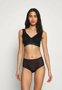 Melna mežģīņu krūšturis ar viļņotu malu, kombinēts ar atbilstošām augsta jostasvieta mežģīņu apakšbiksēm, kurām ir ziedu raksti un maiga tekstūra.