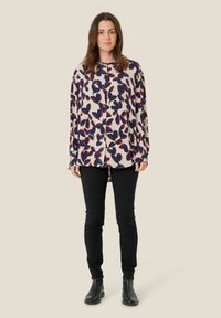 Camicia a maniche lunghe in tessuto leggero, con un motivo floreale in blu navy e rosso su uno sfondo crema, con scollatura tonda e bottoni frontali.