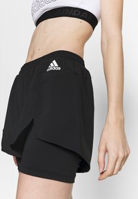Black athletic shorts with an elastic waistband, layered design, and an embroidered white logo. Soft fabric with a smooth texture.
