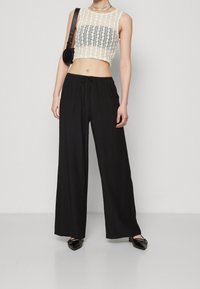 Krátký pletený top v krémové barvě s šedým pruhem; spárován s volnými černými kalhotami s elastickým pasem a šňůrkou. Černé baleríny.