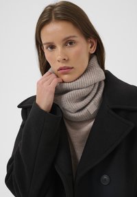 Mustast villast mantel sälgkaelusega ja kahekordsete nuppudega, kombineeritud helebeeži soonikkoes kõrge kaelusega kampsuni ja sobiva kootud kaelusega.