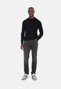 Maglione nero a maniche lunghe con scollo rotondo abbinato a jeans grigi e sneakers bianche e nere, caratterizzato da una vestibilità comoda e texture sottili.