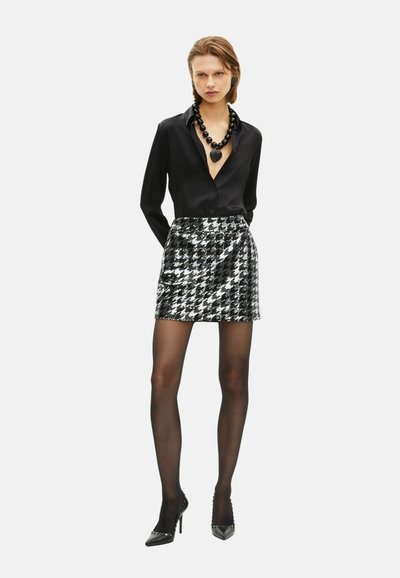 Blusa nera con scollatura a V profonda, abbinata a una mini gonna a fantasia houndstooth bianca e nera. Tacchi alti neri lucidi completano l'outfit.