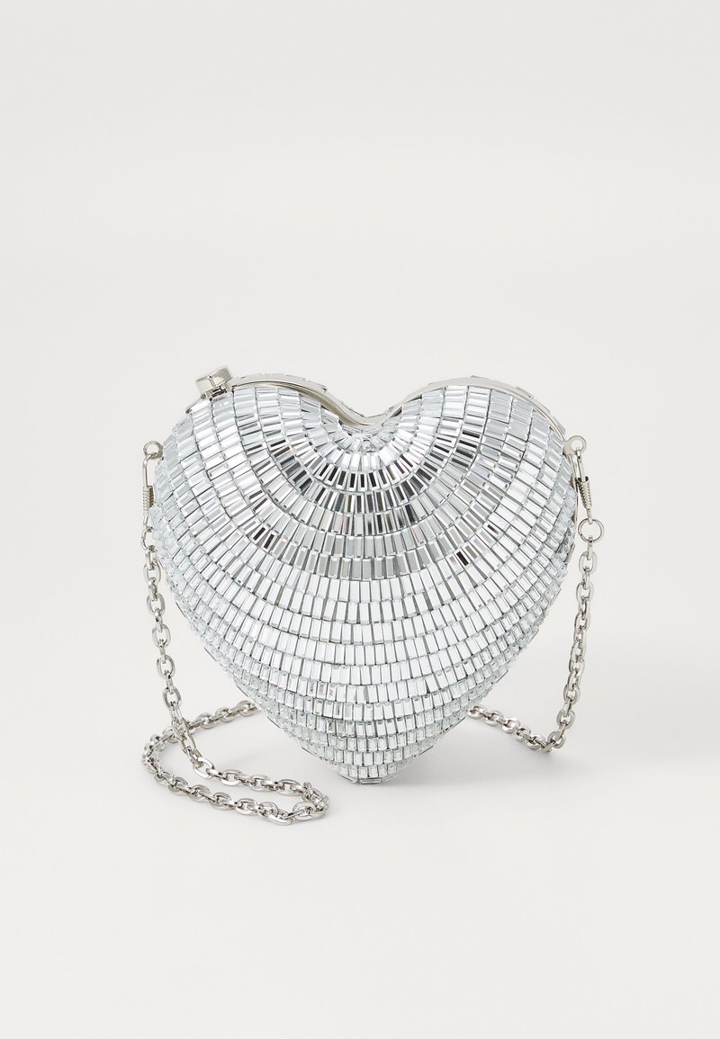Srebrna torebka w kształcie serca, wykonana z lustrzanych płytek, z zamknięciem na zawias i łańcuszkiem. Gładka tekstura z refleksyjną powierzchnią.