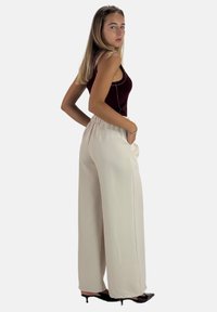 Haut bordeaux sans manches avec un pantalon large beige clair à taille élastique et poches latérales, associé à des talons noirs pointus.