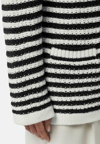 Gestreifter Strickpullover mit abwechselnd schwarzen und weißen horizontalen Streifen, einer strukturierten Oberfläche und einem gerippten Bündchen sowie Taschenakzenten.