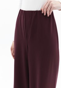 Pantalones de pierna ancha granates con una cinturilla plana y textura suave, que presentan sutiles bolsillos laterales y un acabado limpio en las costuras.