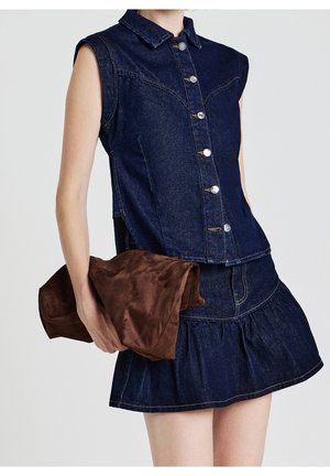 Ærmeløs top i mørk denim med knapper kombineret med matchende denimnederdel med flæsekant, model holder stor brun ruskindsclutch.