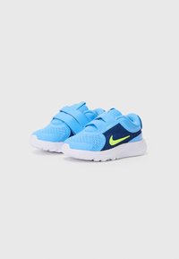 Chaussures de sport bleues avec une tige en maille, des bandes Velcro et des accents noirs. Elles présentent une semelle en caoutchouc blanche et un logo vert fluo sur le côté.