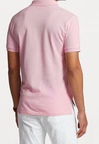 Rosa pikétröja med strukturerad textil, korta ärmar och klassisk krage, visad bakifrån, kombinerad med vita byxor.