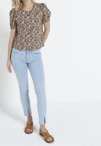 Floral print top with puff sleeves in shades of pink and green, paired with light blue skinny jeans featuring ankle slits and brown sandals.