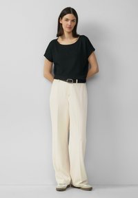 Top corto de manga corta negro texturizado combinado con pantalones de talle alto de pierna ancha crema y zapatos beige de deslizar con suelas blancas.