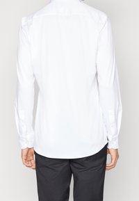 Witte langekleurige shirt met een breed kraag, knoopmanchetten, een gladde textuur en een gebogen zoom. Achteraanzicht met minimale ontwerpdetails.