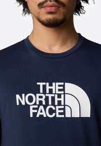 Navy blue cotton t-shirt featuring a bold white logo design that includes text and a half-circle graphic. Soft texture and crew neck shape.