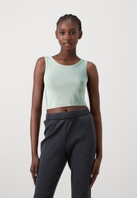 Mintgrønn ribbet cropped tanktop kombinert med mørkegrå, teksturert ribbet bukser. Antrekket har en enkel, rund halslinning.