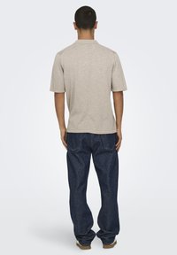 Camisa corta de manga corta en color beige claro con un ajuste relajado, combinada con pantalones de mezclilla azul oscuro. El tejido parece suave, con una textura lisa.