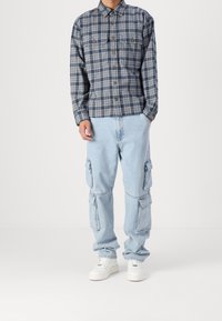 Camisa de cuadros abotonada en azul marino y azul claro, combinada con pantalones cargo azul claro con bolsillos laterales y zapatillas blancas.