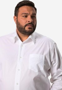 Camicia bianca con colletto, tasca e maniche lunghe. Realizzata in tessuto morbido con una trama sottile, presenta bottoni trasparenti.