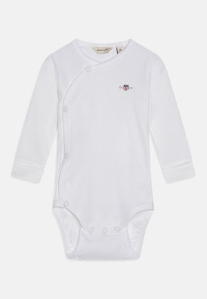 Bodysuit blanc à manches longues en tissu doux, avec une fermeture à pressions diagonale et un petit emblème coloré sur la poitrine.