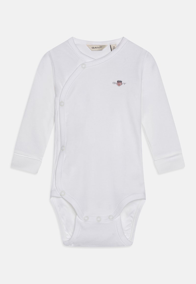 Hvit langermet bodysuit laget av myk tekstil, med skrå trykknapp-lukking og et lite farget emblem på brystet.